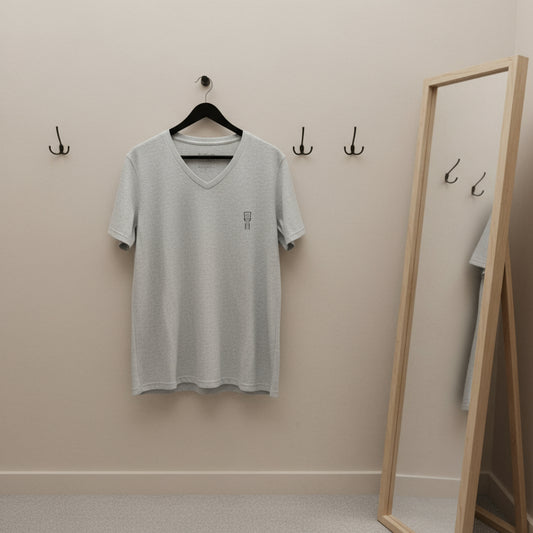 Gray t-shirt hanging on a hanger against a beige wall with a mirror and hooks.