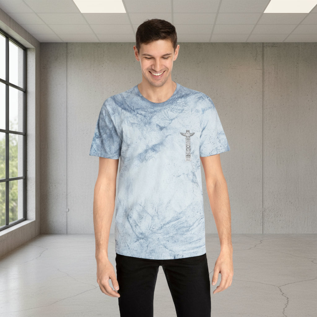 Person wearing a light blue tie-dye t-shirt with a logo in a room with large windows.