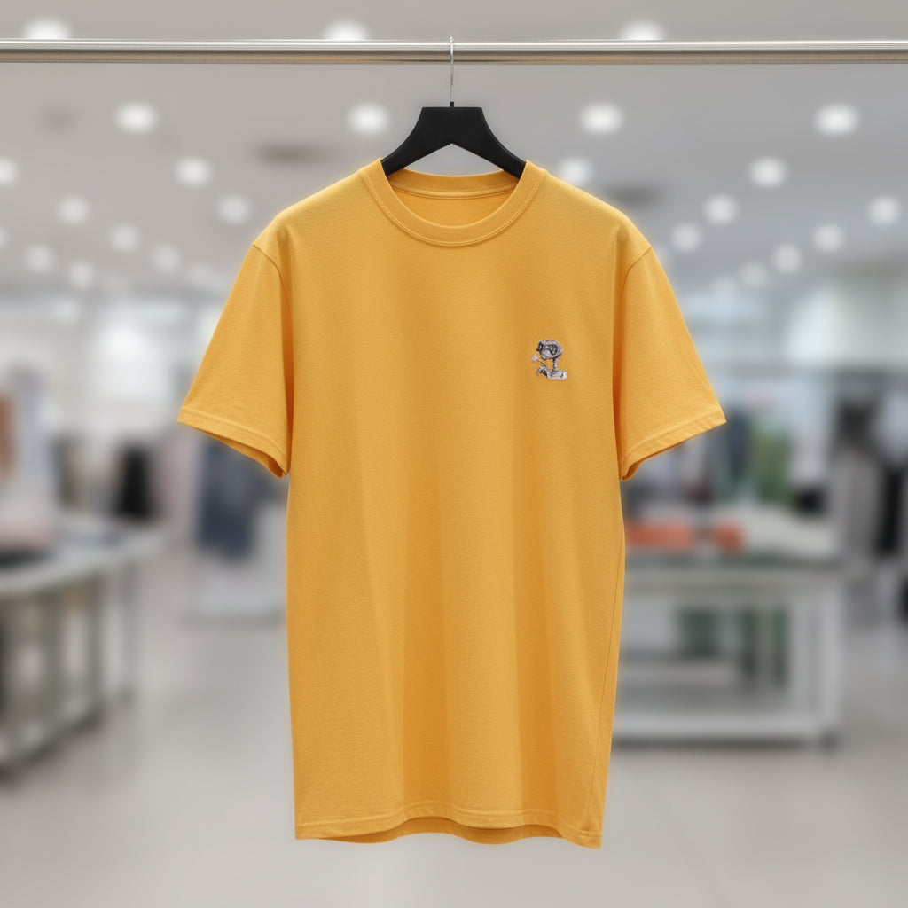 Yellow t-shirt with a small logo on a hanger against a blurred indoor background