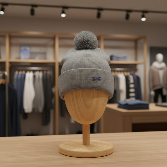 Gray beanie with a pom-pom on a wooden mannequin head in a clothing store setting.