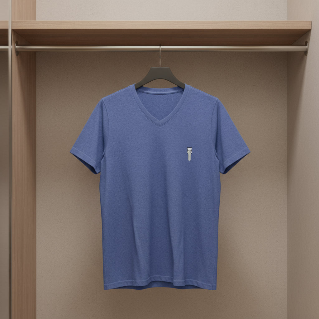 Blue t-shirt with a small logo on a hanger against a beige wall.