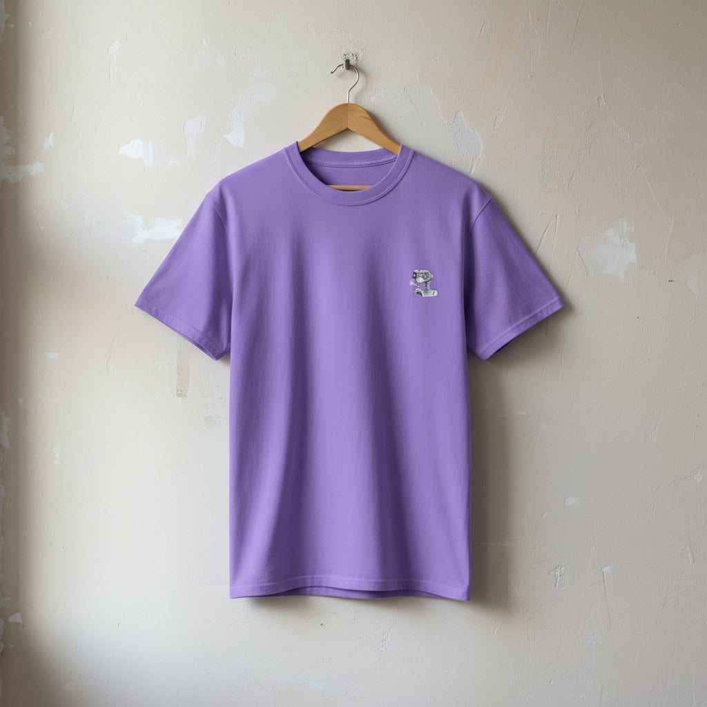 Purple t-shirt with a small logo on a hanger against a beige wall.